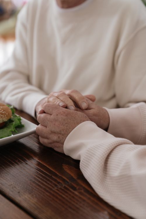 Free A close-up of two adults holding hands across a wooden table, creating a warm, intimate moment. Stock Photo