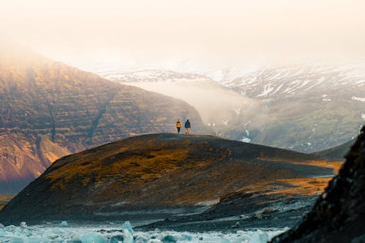 Two hikers traverse a scenic, snow-capped mountain landscape in Iceland.