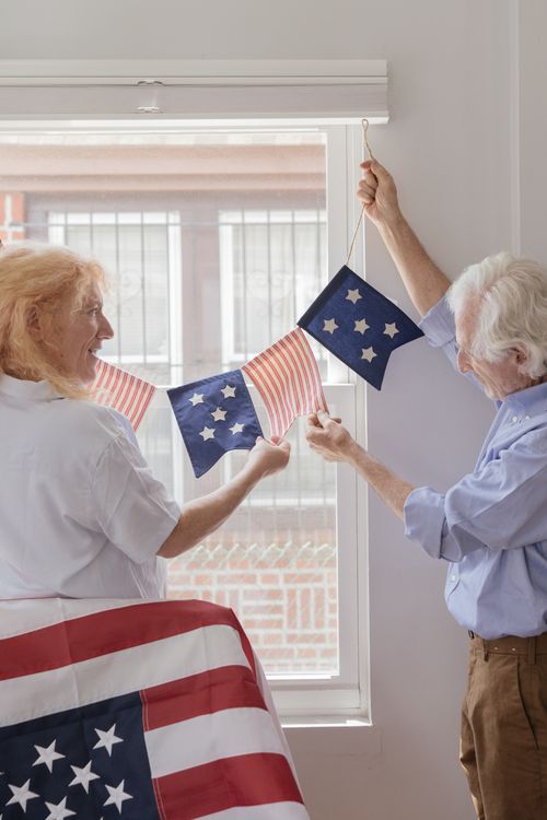 Free Joyful senior couple hanging patriotic American flag buntings indoors, celebrating together. Stock Photo