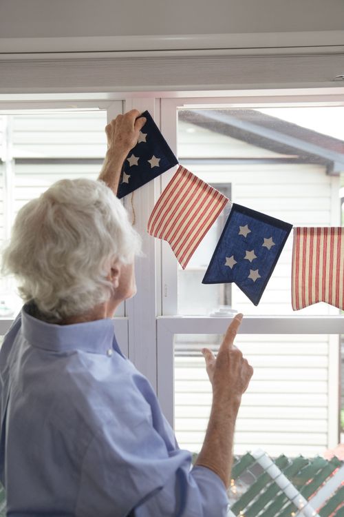 Free An elderly person decorates a window with American flag-themed bunting on Independence Day. Stock Photo