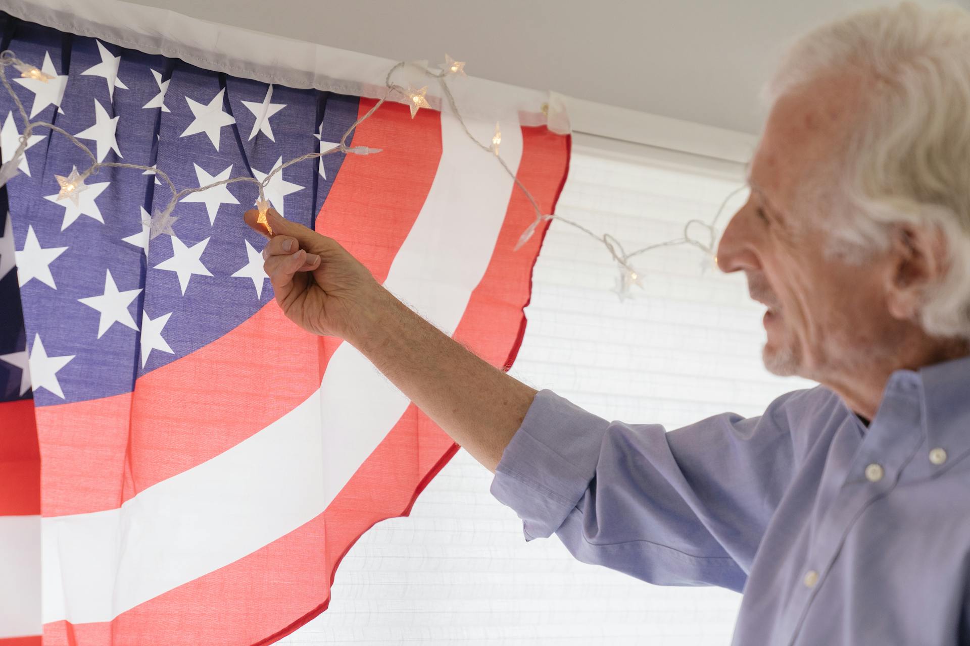 Senior adult decorating with American flag and lights for celebration indoors.