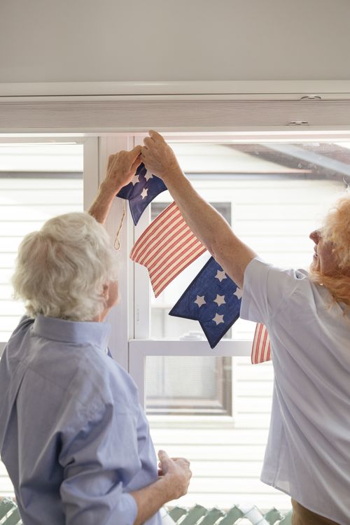 Free Elderly couple hanging American flag-themed decorations for a patriotic celebration indoors. Stock Photo