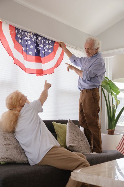 Free Senior couple decorating with American flag, celebrating Independence Day together indoors. Stock Photo