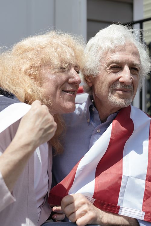 Free Elderly couple wrapped in American flag enjoying a sunny outdoors day. Stock Photo