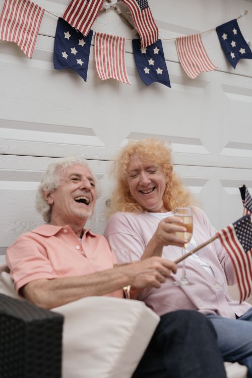 Free Joyful senior LGBT couple celebrating the 4th of July with American flags and laughter. Stock Photo