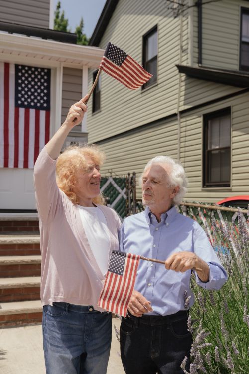 Free Senior couple joyfully celebrating with American flags on Independence Day outdoors. Stock Photo