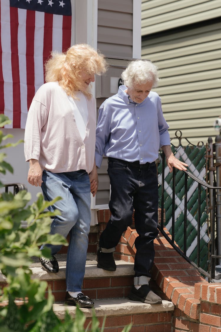 Woman Assisting An Elderly Man Going Down The Stairs