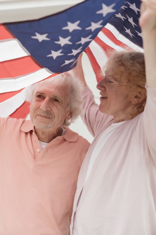 Free Elderly couple joyfully holding a waving American flag outdoors. Stock Photo