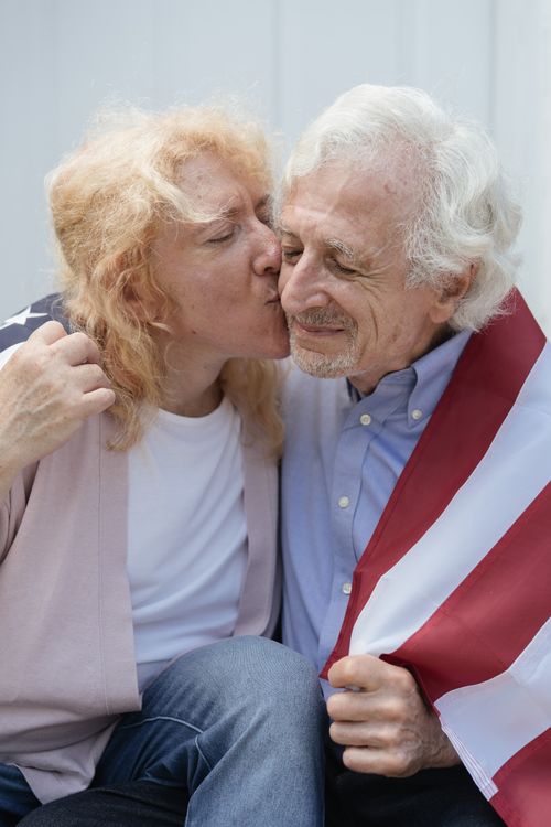 Free Senior couple showing affection, wrapped in American flag, symbolizing love and patriotism. Stock Photo