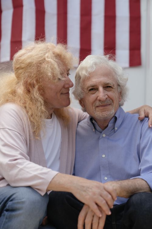 Free Elderly couple sharing a warm embrace in front of an American flag, symbolizing love and patriotism. Stock Photo