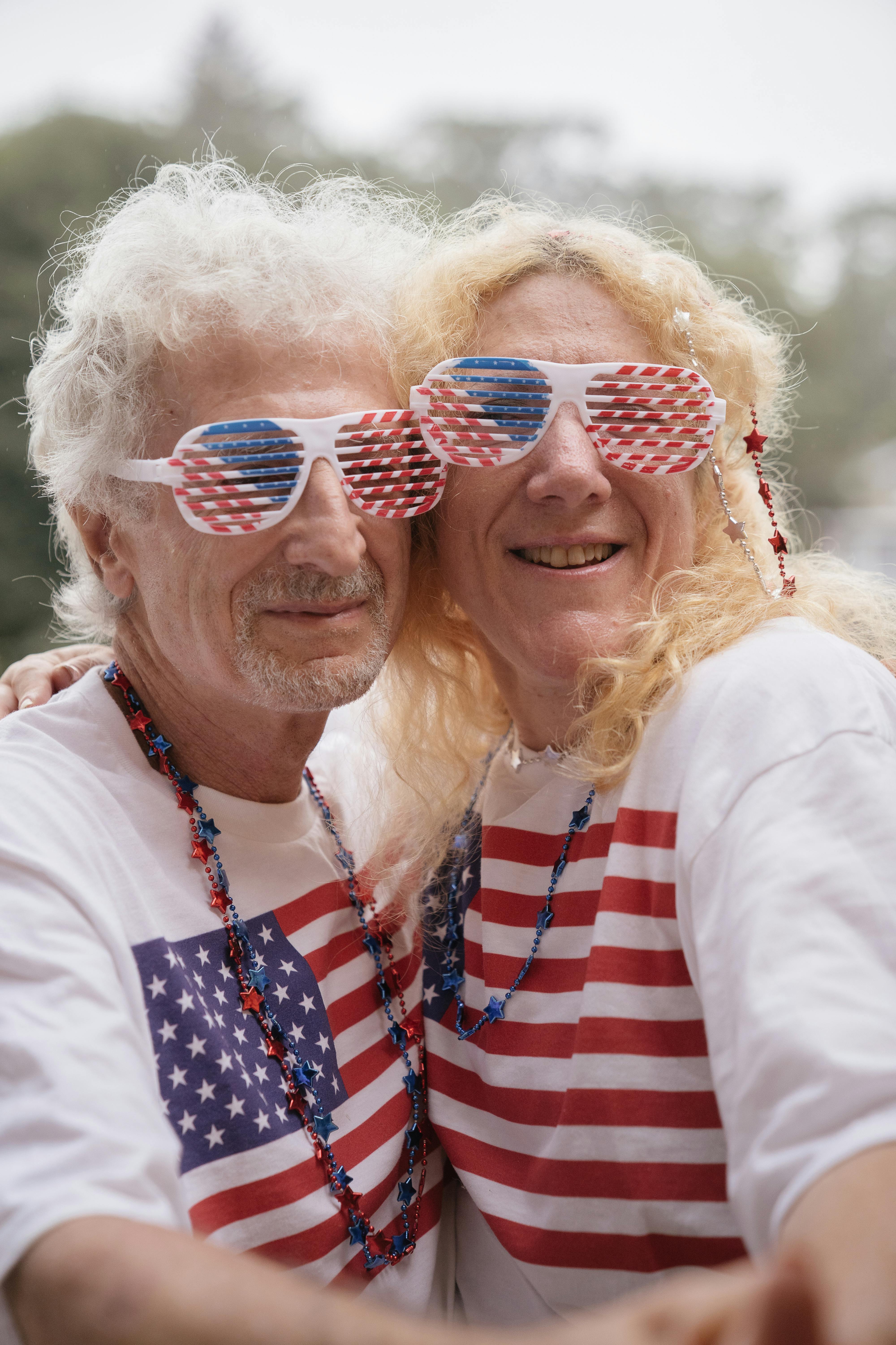 Happy senior couple wearing American flags celebrating Independence Day outdoors.