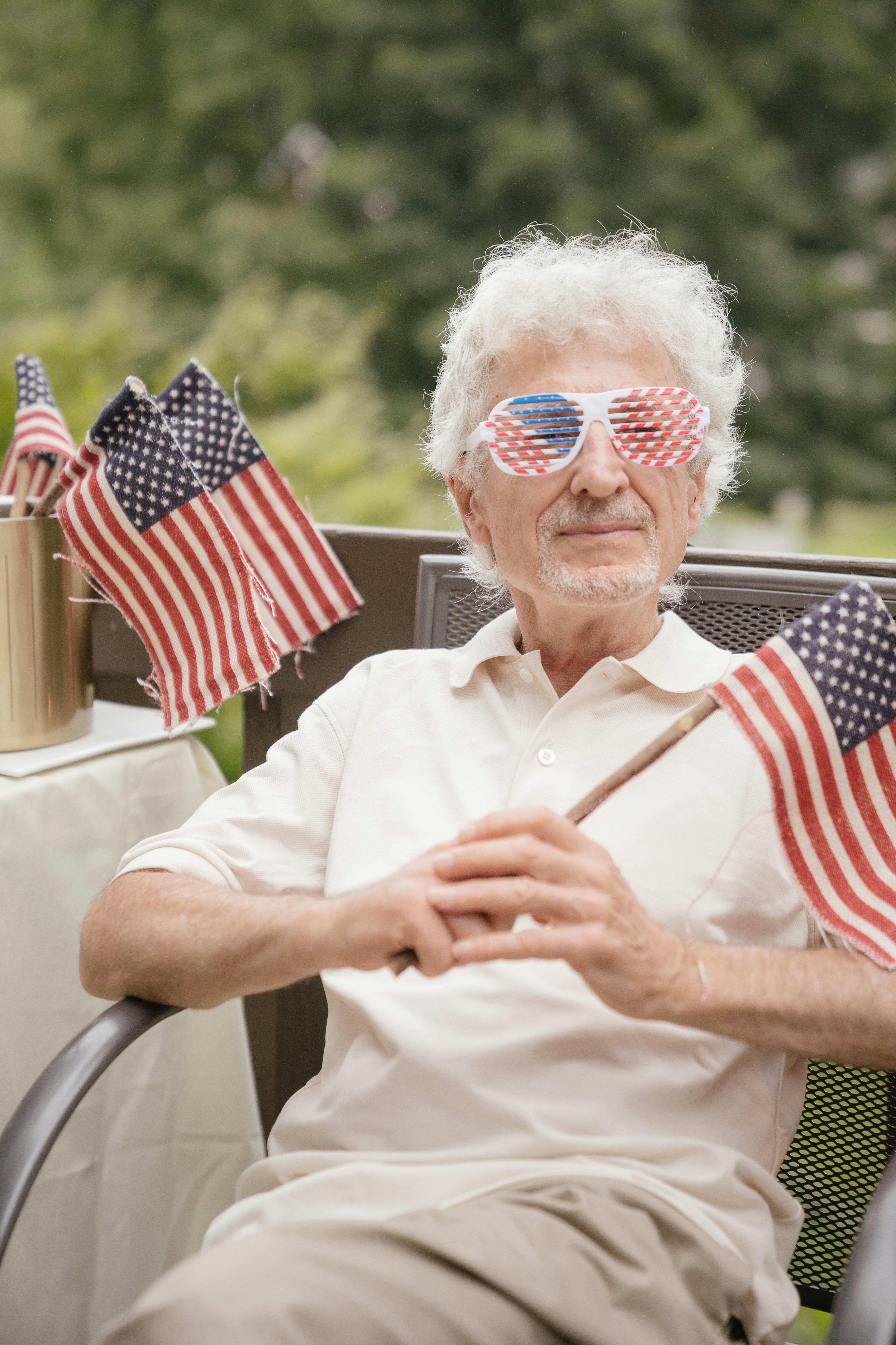 Elderly man with American flag sunglasses celebrating Independence Day outdoors.