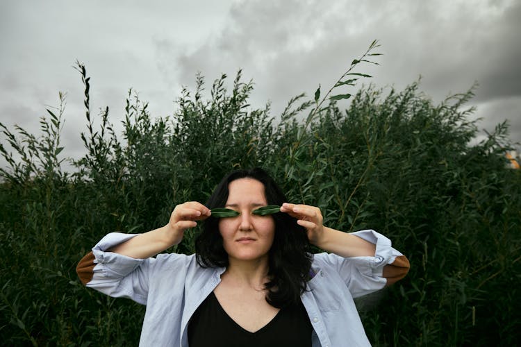 A Woman Covering Her Eyes With Two Green Leaves