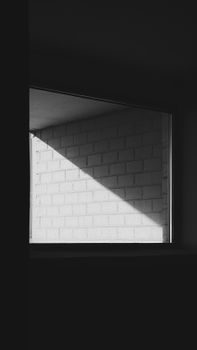 Monochrome image of shadow and light interplay on a brick wall viewed through a window, offering a minimalist architectural study.