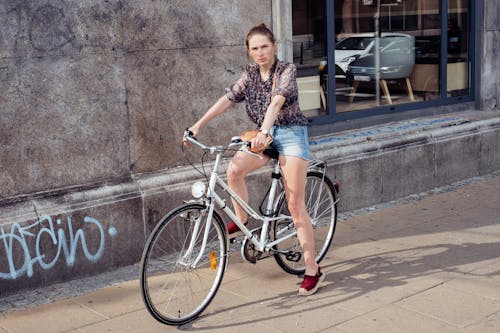 Photo of a Woman in Denim Shorts Riding a White Bicycle