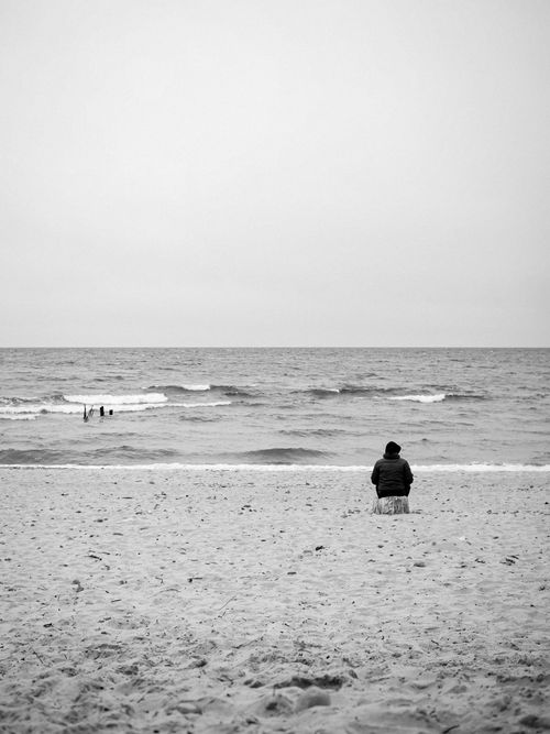 Free Black and white image of a person sitting alone on a Kaliningrad beach, facing the ocean. Stock Photo
