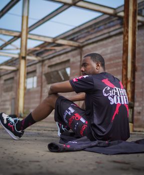 African American man in trendy urban clothing sitting in an industrial setting.