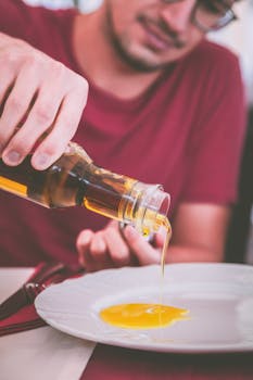 Man pouring olive oil onto a plate indoors, perfect for culinary and healthy eating themes.