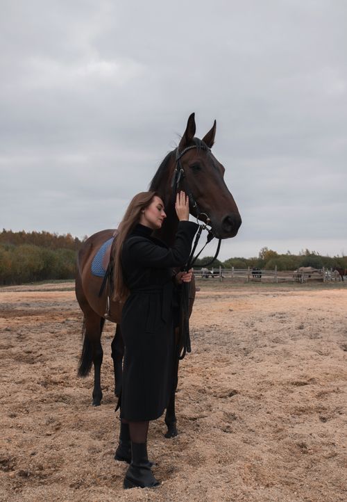 Free A woman in black stands beside a horse in an outdoor stable setting. Stock Photo