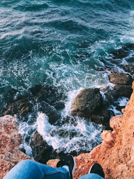 Dramatic view from a cliff edge over a rocky coastline with crashing waves.