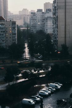 View of a rainy urban street with tall buildings and parked cars showcasing modern architecture.