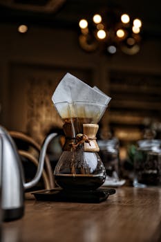 Creative close-up of a coffee dripper in a warm cafe setting, featuring rustic and vintage elements.