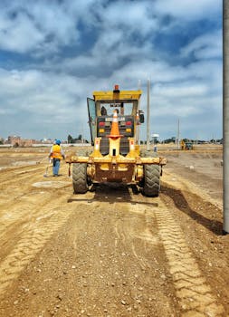 Motor grader on a construction site preparing dirt ground on a sunny day.