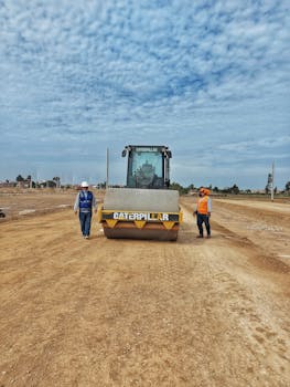 Construction workers with Caterpillar machinery on a dirt road under a cloudy sky.