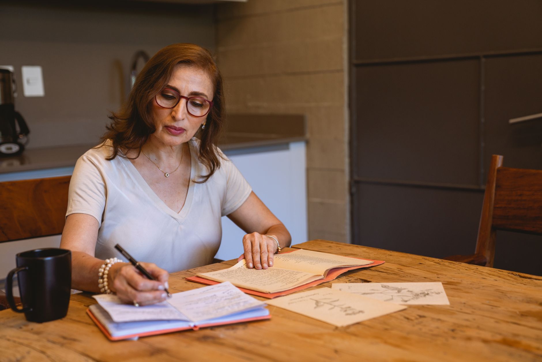 A person writing in a journal at a kitchen table in morning light, the daily check-in done on paper