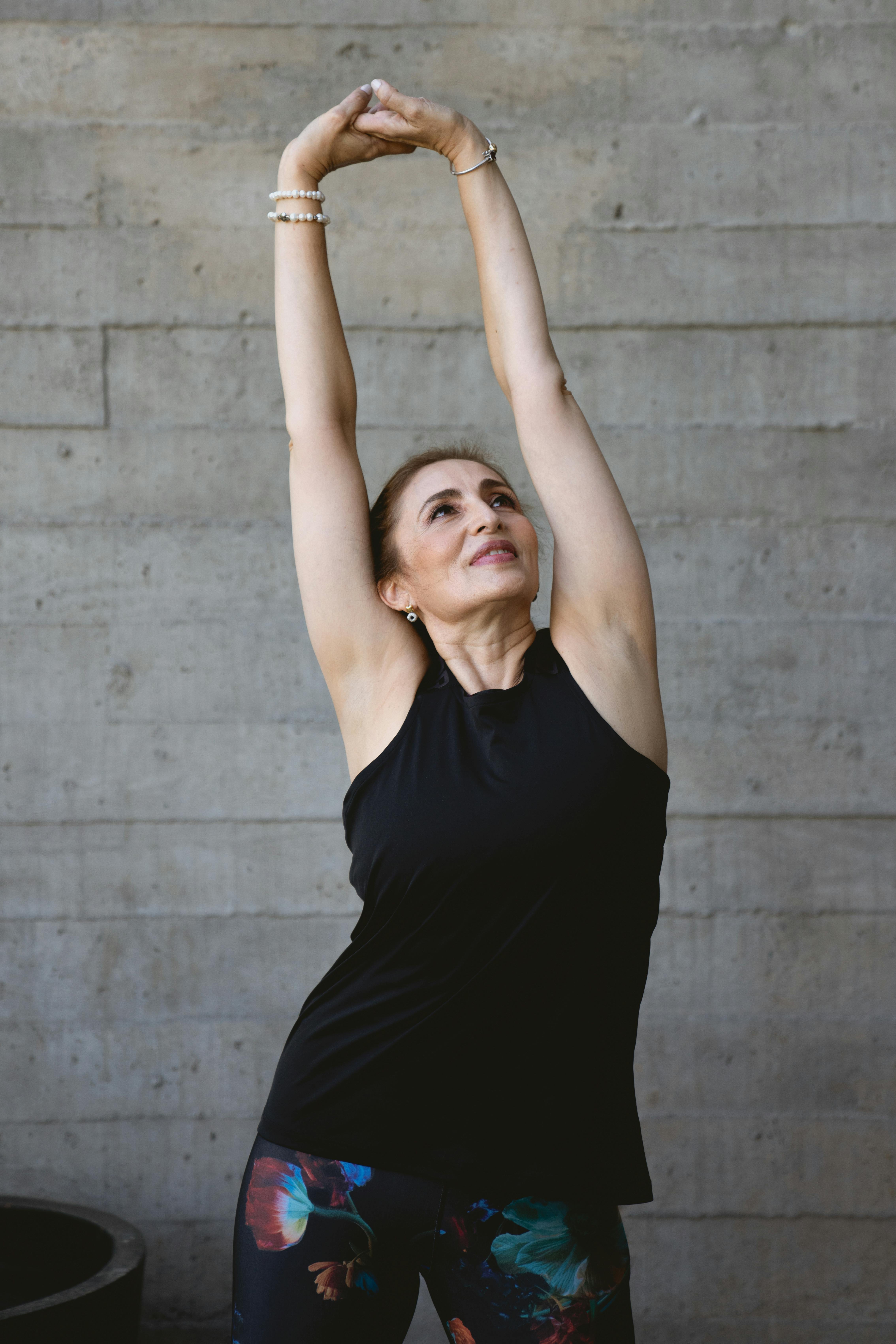 Elderly woman in black tank top stretching indoors for fitness and positive aging.