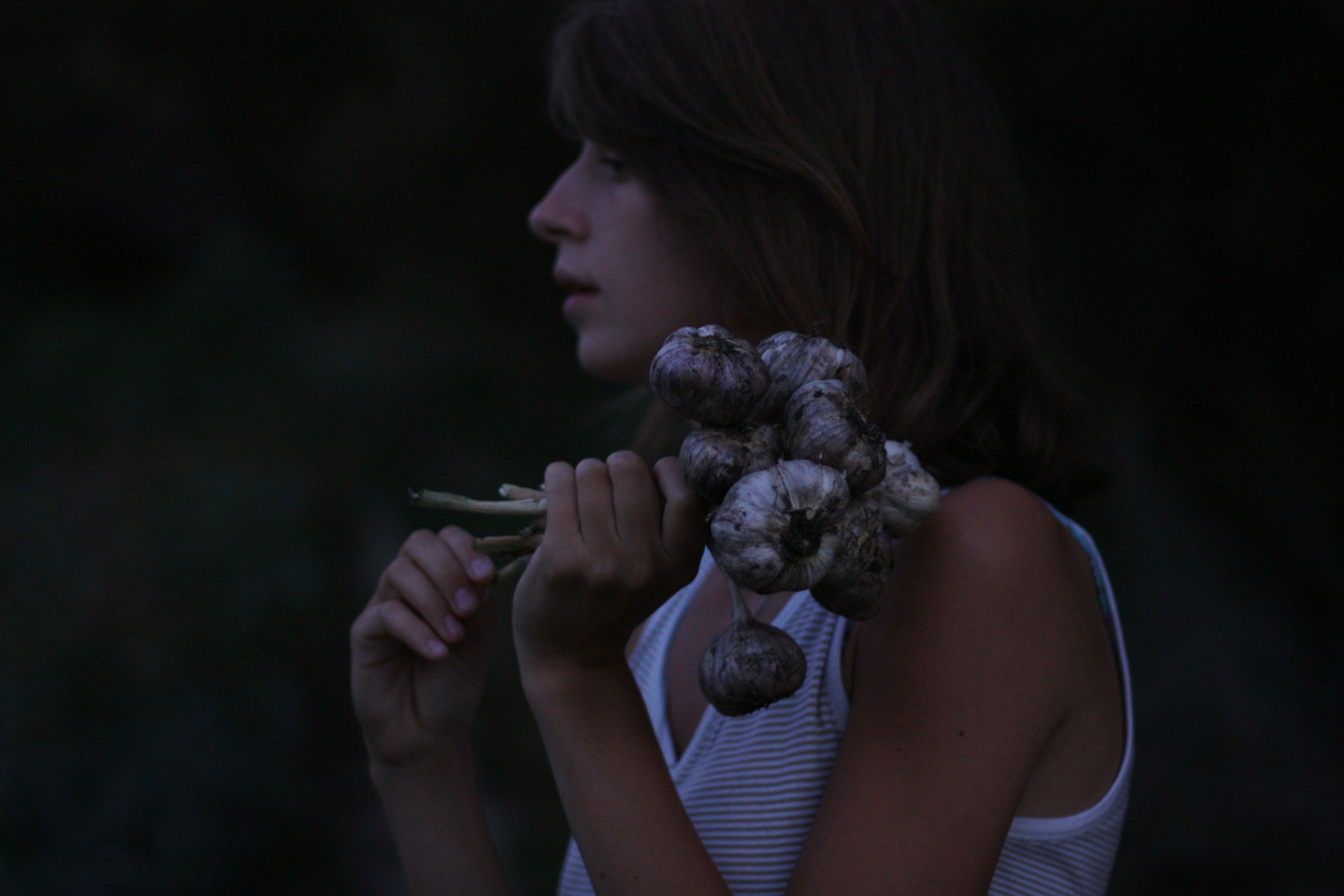 A woman holding garlic, captured in a moody, natural light setting.