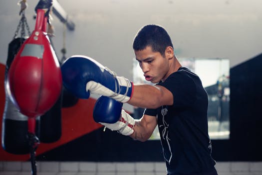 A determined boxer trains with a punching bag in a boxing gym, wearing gloves and sportswear.