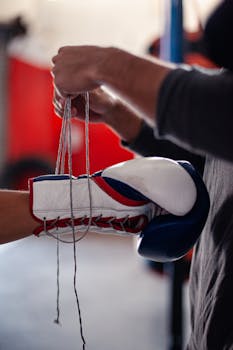 A detailed view of a boxing glove being tied on a boxer's hand in a gym setting.