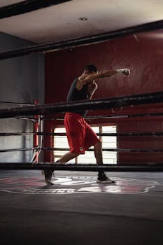 Man practicing shadowboxing in an indoor boxing ring with moody lighting.