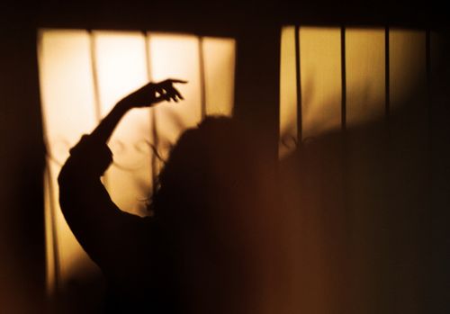 Free Silhouette of a person lifting hand against a window with warm sunlight creating dramatic shadows. Stock Photo