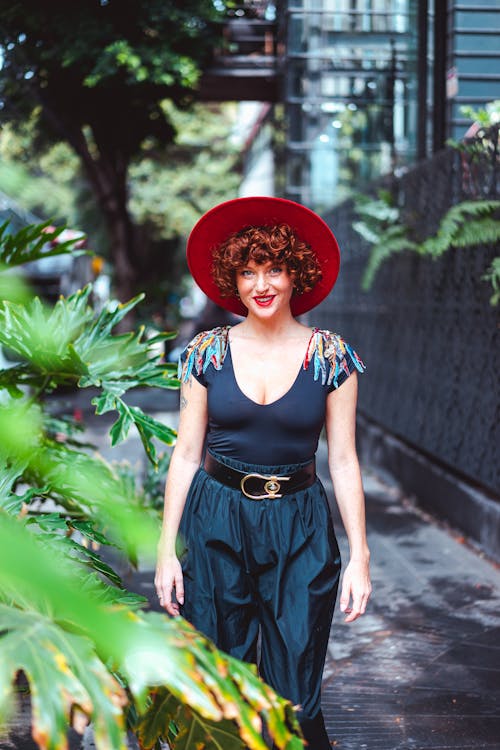 Woman Wearing Hat Standing near Plants on Sidewalk