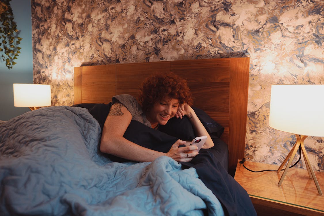 Close-Up Shot of a Woman Holding a Smartphone while Lying Down on Bed