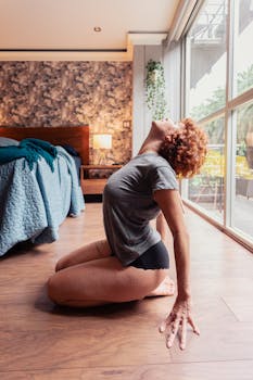 A woman with curly red hair performs yoga indoors by a large window.