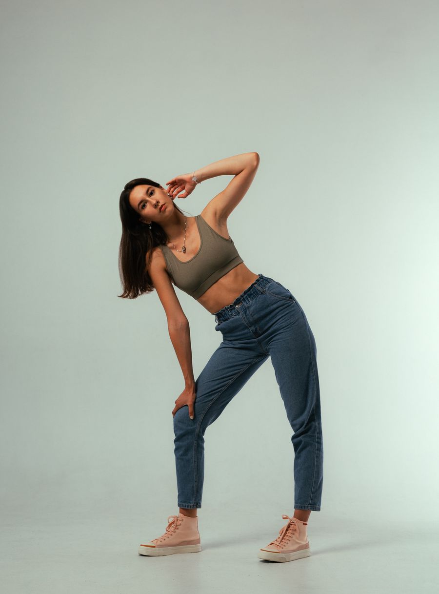 Model in a cropped top and straight-leg jeans posing against a soft green studio backdrop — photo by Alexandr on Pexels