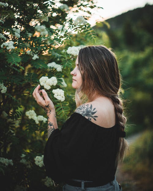 A Woman in Black Off Shoulder Top Looking at White Flowers