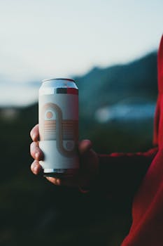 Close-up of a hand holding a designer soda can with blurred outdoor background.