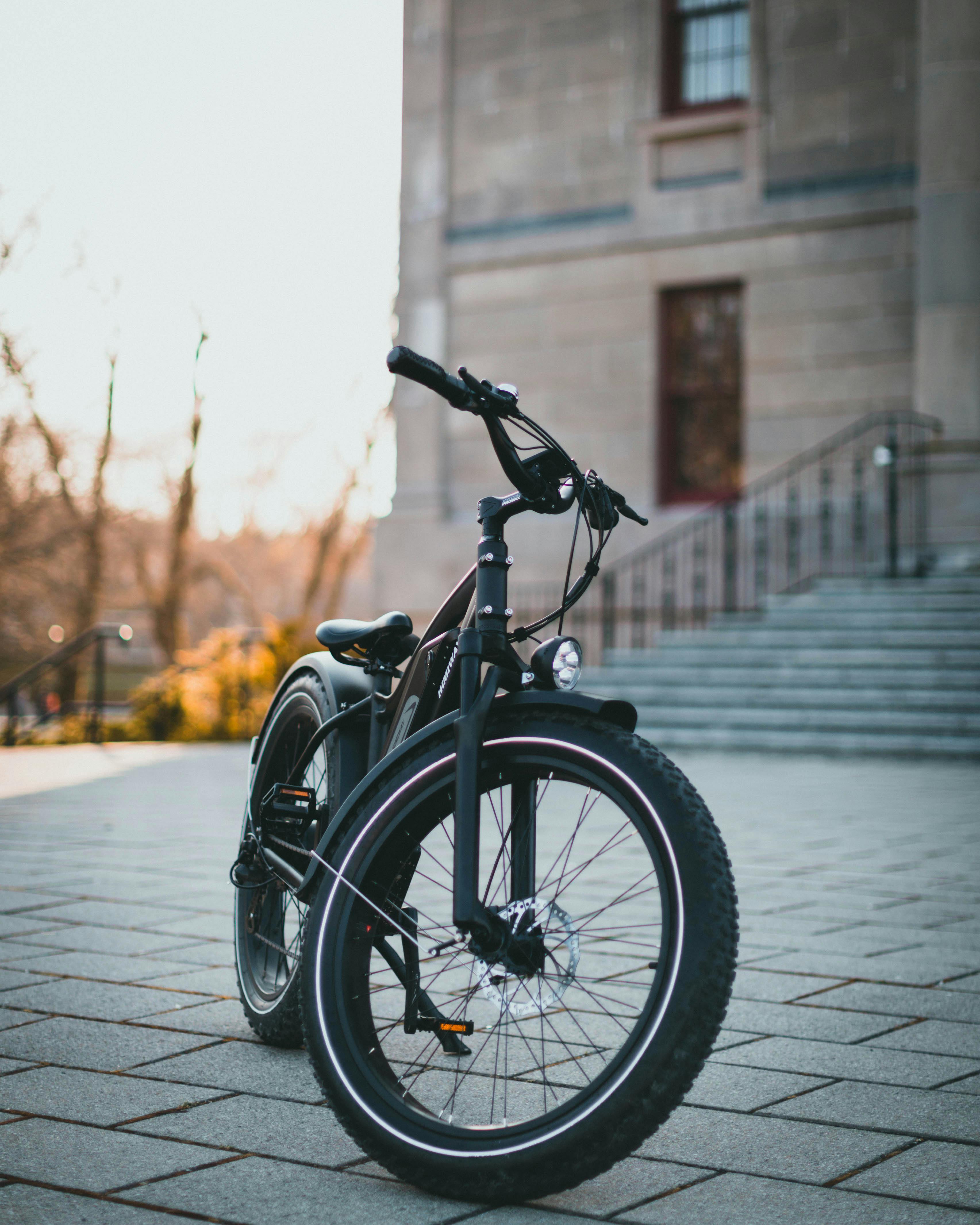 Free A black bicycle parked on a concrete pavement in front of a historic building facade. Stock Photo