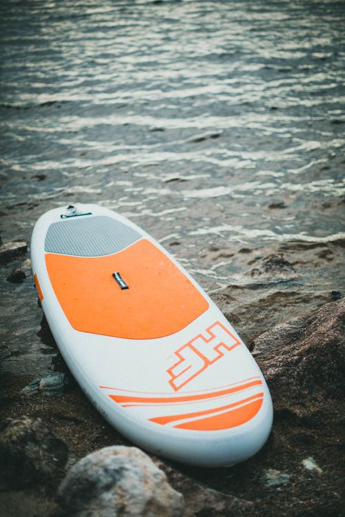 Free A paddleboard lying on rocky shore with serene water backdrop, ideal for aquatic sports themes. Stock Photo