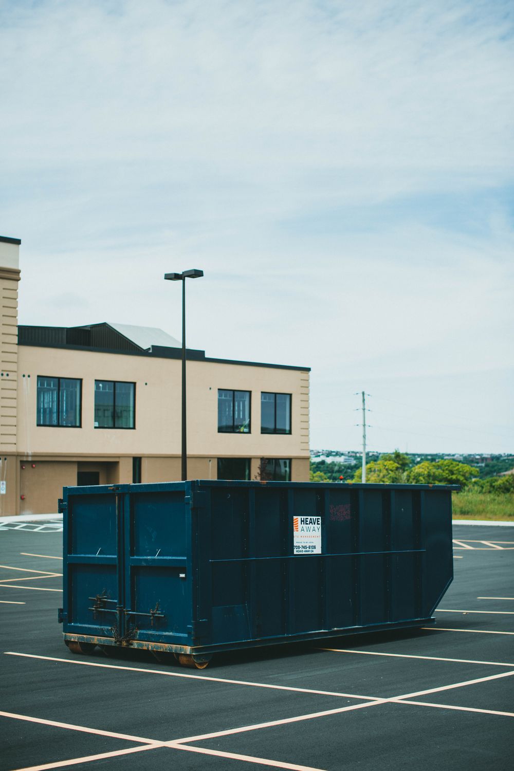 Large roll-off dumpster container parked on pavement next to a delivery truck