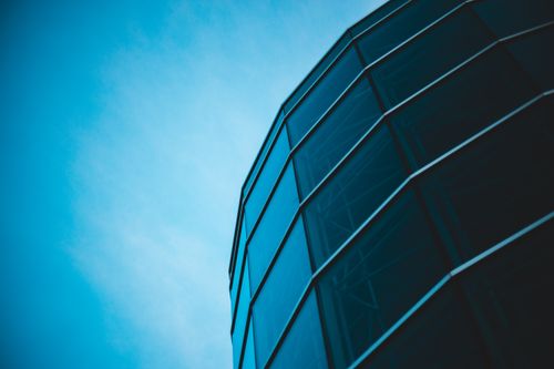 Free Low-angle view of modern glass architecture set against a bright blue sky, offering a minimalist and sleek design perspective. Stock Photo