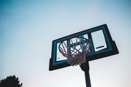 A low-angle view of a basketball hoop and backboard against a clear sky during dusk.
