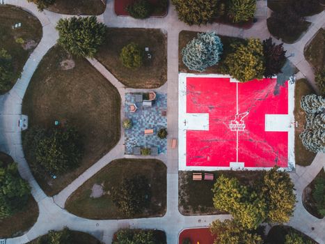 Aerial view of a beautifully designed park featuring a vibrant red sports court surrounded by lush greenery.