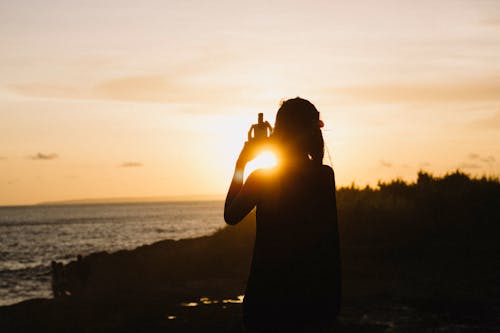 Free Silhouette of Woman Standing Near Body of Water during Sunset Stock Photo