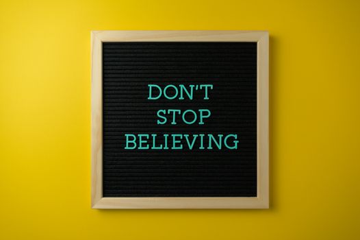 Inspirational message 'Don't Stop Believing' on a letter board against a vibrant yellow background.