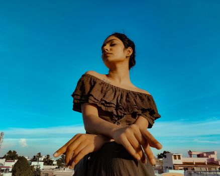 A woman confidently poses outdoors in an off-shoulder top with a vibrant blue sky backdrop.